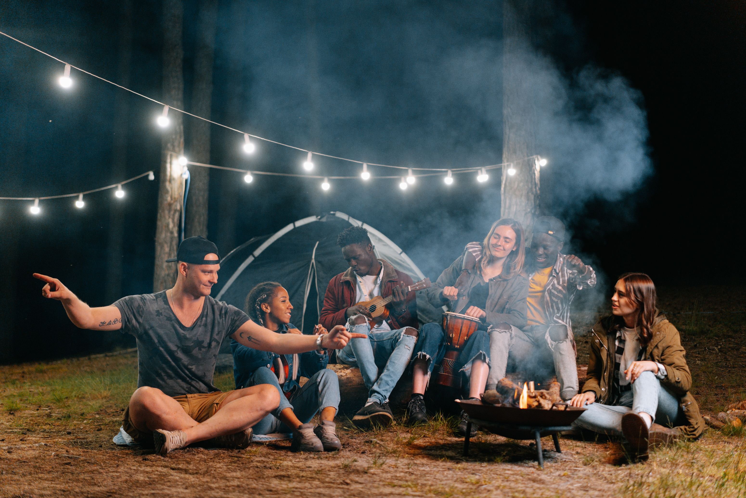 Friends relaxing by a campfire in the forest, playing music and talking on a camping trip