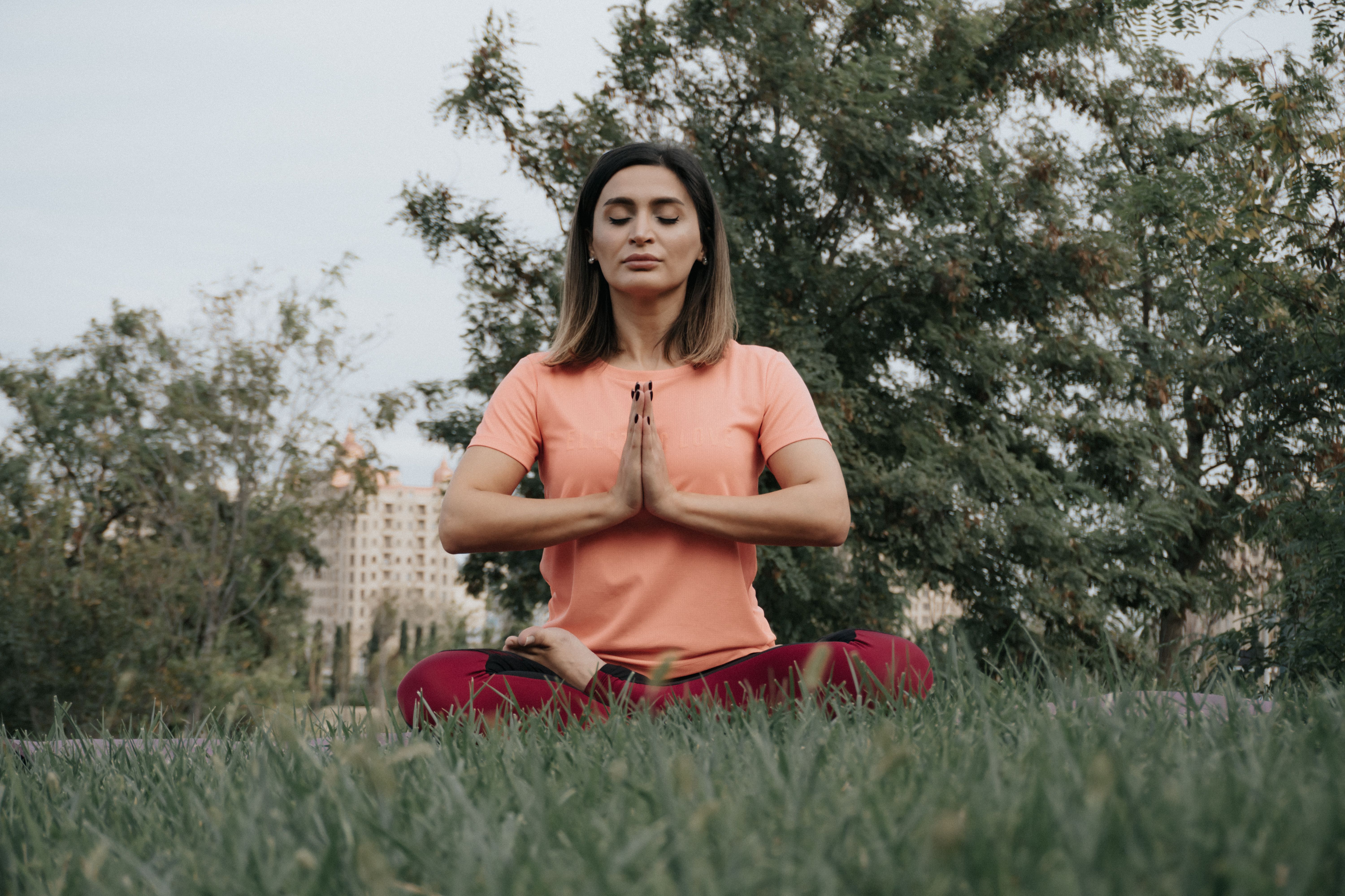 Woman practicing yoga and meditation in a park, enhancing mindfulness and wellness outdoors