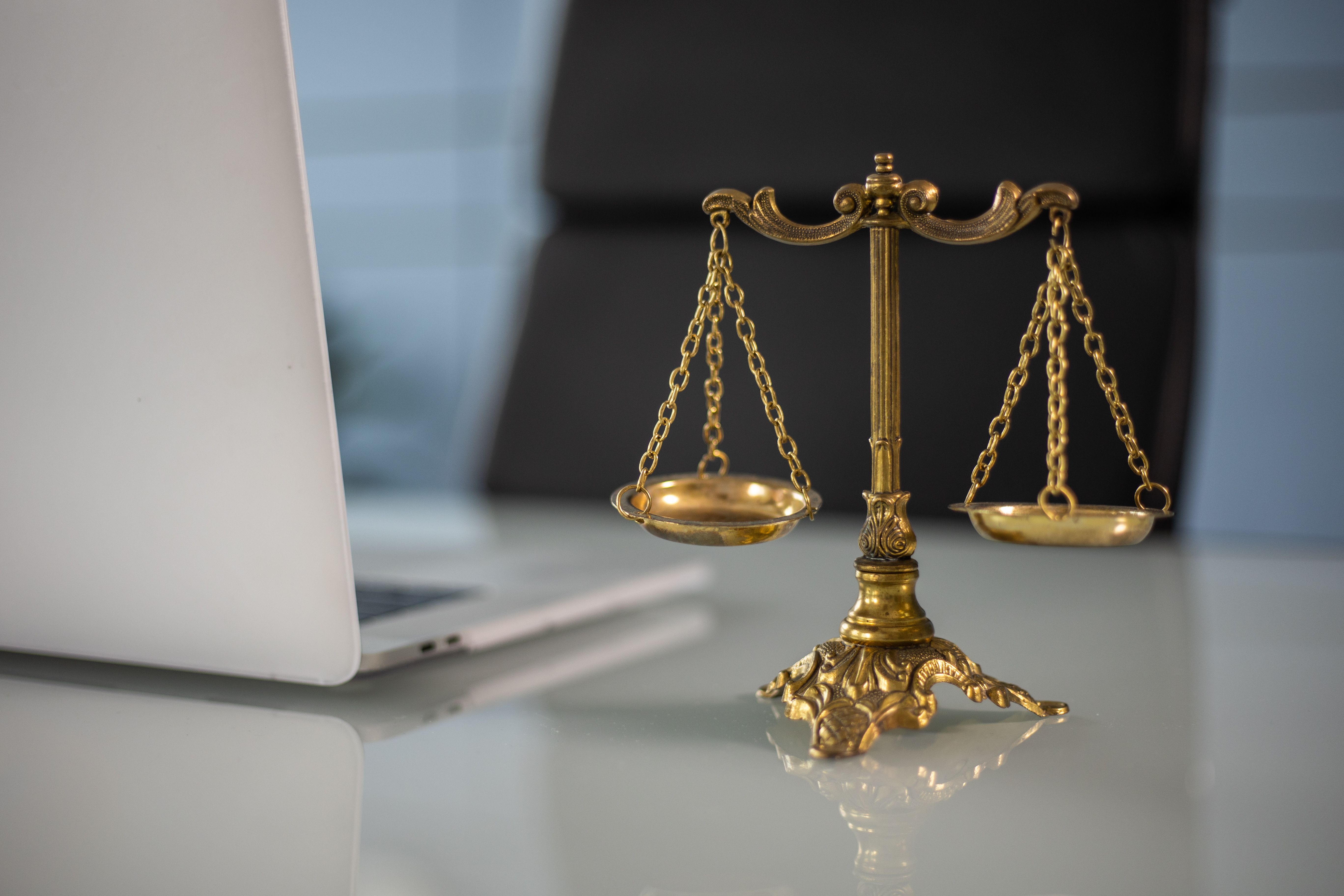 Golden justice scales on a desk beside a laptop, symbolizing law and balance